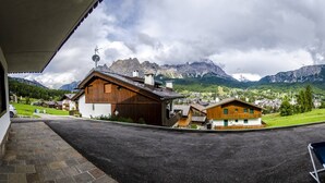 Blick von einer überdachten Veranda auf ein Bergdorf mit Holzhäusern und blauem Himmel.