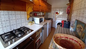 Eine kompakte Küche mit Gasherd, Mikrowelle und Waschmaschine. Es gibt Holzschränke und eine geflieste Spritzschutzwand.