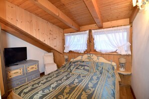 A wooden-paneled room with a bed, a dresser, a television, and two windows with curtains.