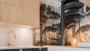 Une cuisine moderne avec un plan de travail en marbre, des meubles noirs et blancs, et une fresque représentant des arbres.