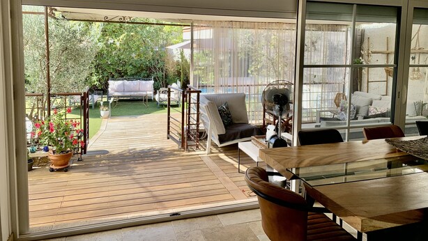 A modern patio with a wooden deck, a glass table, and a seating area with a sofa and chairs. - Maison Avec Piscine (Saint-Raphaël)