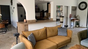A modern living room with a sofa, coffee table, and a kitchen area visible through an archway. - Maison Avec Piscine (Saint-Raphaël)