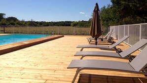 Een houten terras met een zwembad, ligbedden en een parasol.