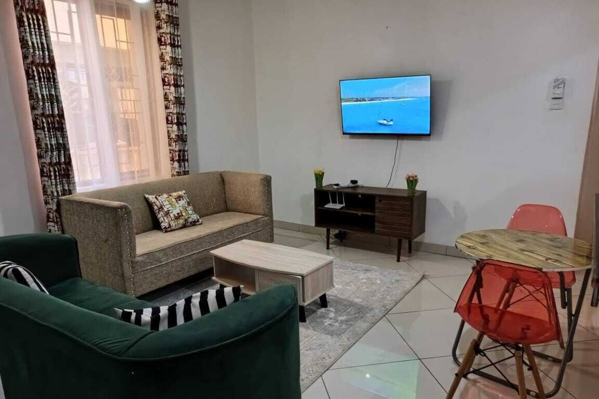 A living room with a sofa, a coffee table, a TV mounted on the wall, and a small dining table with chairs.