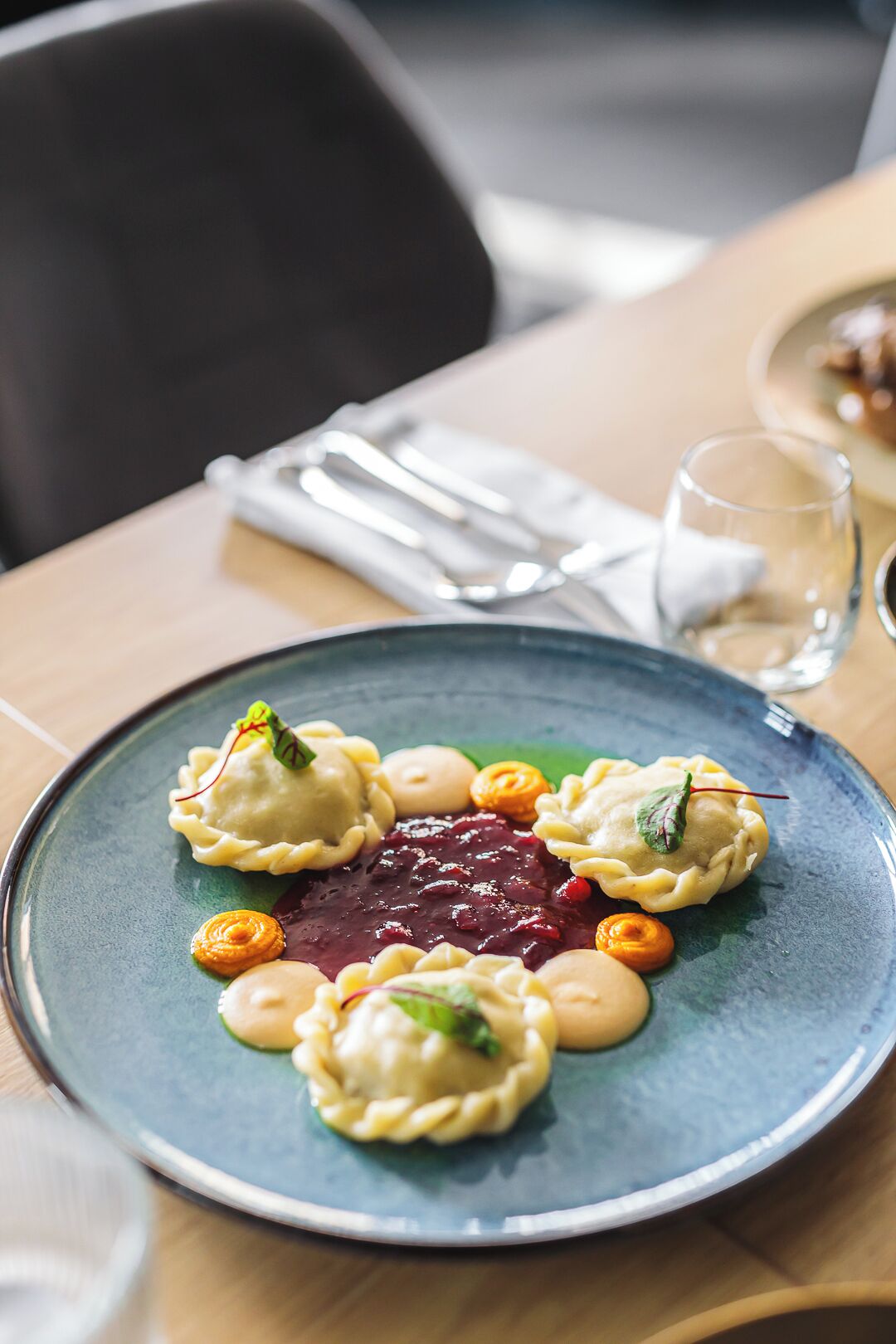 A plate of dumplings with a berry sauce and garnishes on a blue ceramic plate.