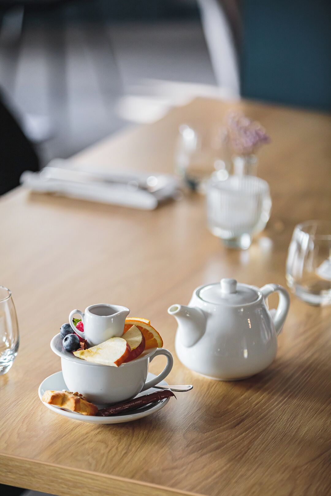 Une table avec une théière, une tasse et sa soucoupe, une assiette contenant de la nourriture et un sachet de thé.