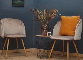 Deux chaises modernes aux pieds en bois et une petite table ronde, entre lesquelles se trouve un vase de fleurs séchées.