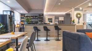 Zona de bar moderna con mostrador de madera, taburetes negros y un espacio de descanso con sofá azul y una silla amarilla.