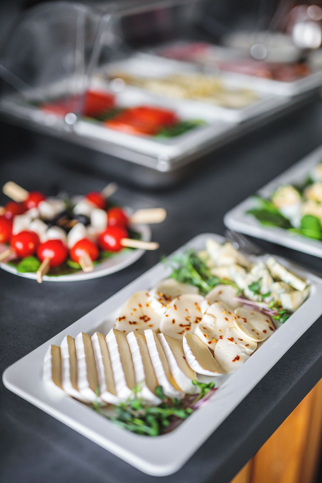 Un bufé con diversos platos, incluyendo tomates brochetas, queso en rodajas y una ensalada.