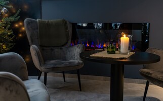 Un coin salon chaleureux avec une cheminée, un sapin de Noël et une bougie sur une table.