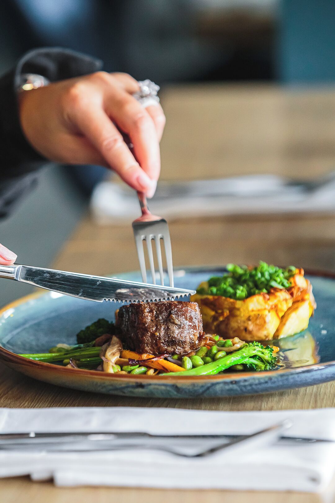A person using a fork to eat a steak with vegetables on a plate.