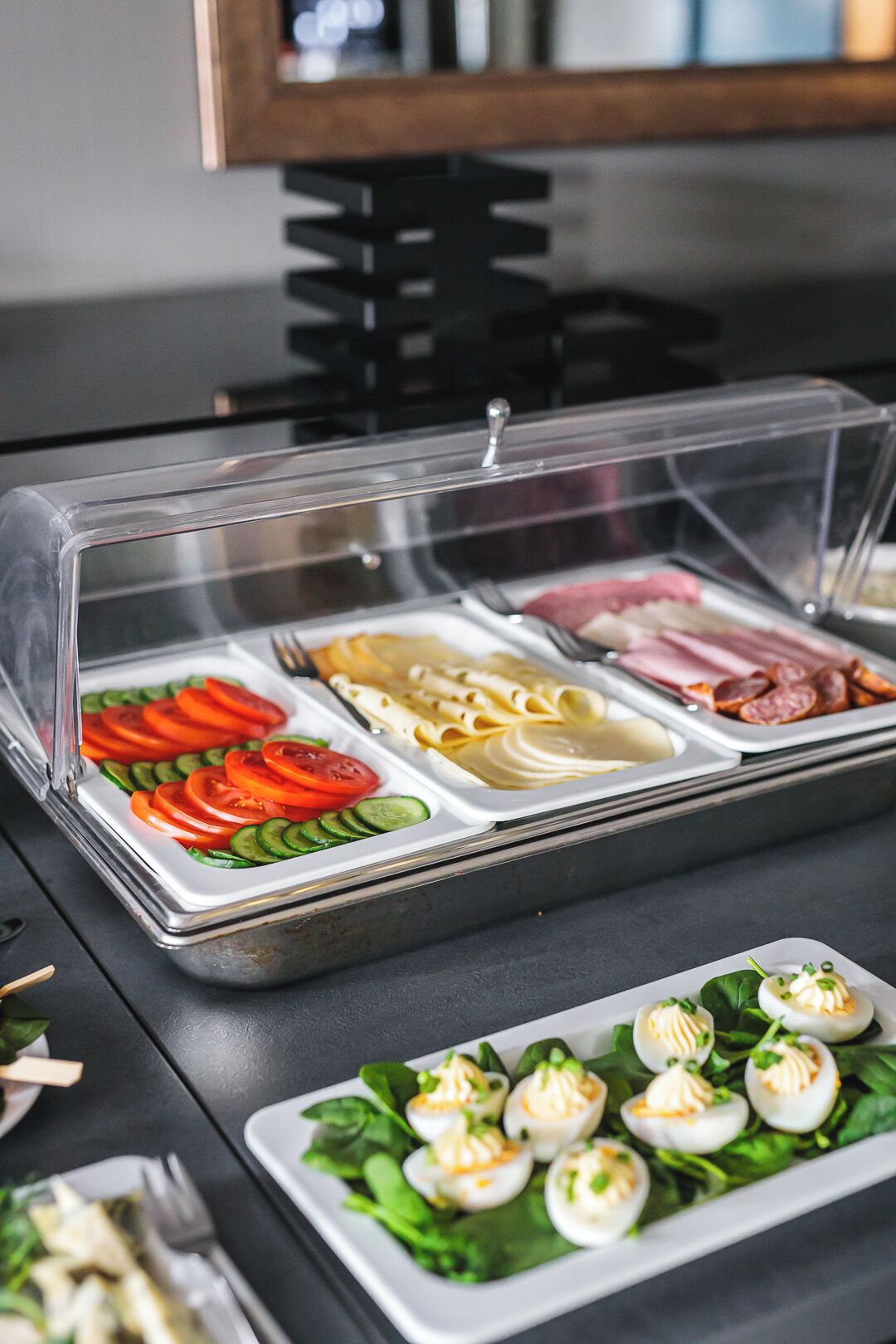 A buffet with various food items including sliced tomatoes, cucumbers, pasta, and meats.