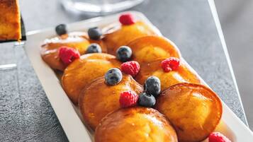 A plate of glazed donuts with blueberries and raspberries, and a bowl of assorted fruits in the background.