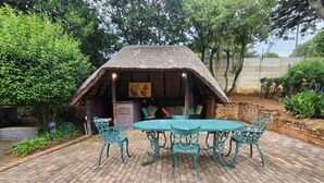 Une construction à toit de chaume, avec une table et des chaises, située dans un jardin.