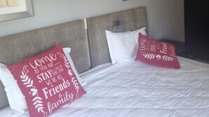 Une chambre d’hôtel avec un lit, deux oreillers ornés d’inscriptions et deux tableaux encadrés accrochés au mur.