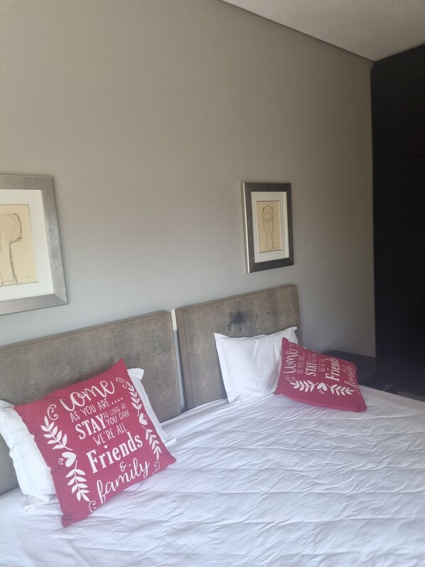 A hotel room with a bed, two pillows with text, and two framed pictures on the wall.