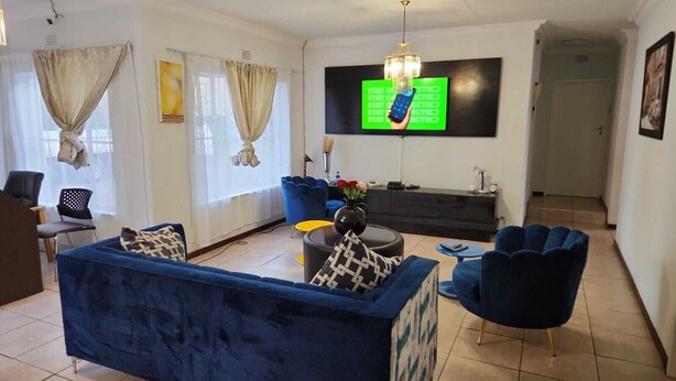 Un salon avec un canapé bleu, un fauteuil bleu et une petite table ronde sur laquelle est posé un vase de fleurs. Un téléviseur est fixé au mur et un lustre est suspendu au plafond.