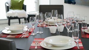 A dining table set with multiple wine glasses, plates, and cutlery, with a chair and a green pillow in the background.
