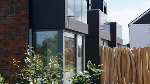 A modern building with a brick facade, large windows, and a wooden fence in the foreground.