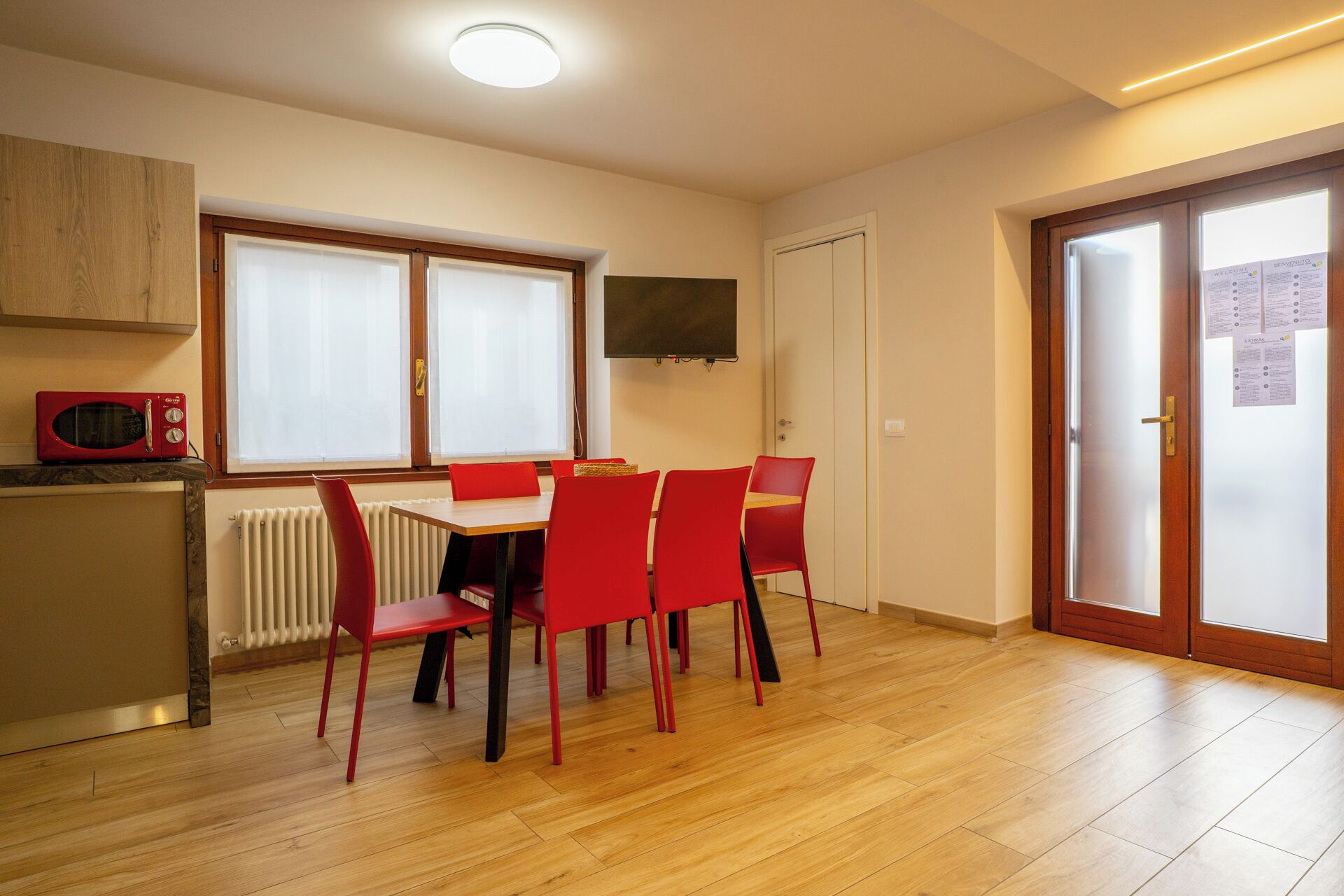 Comedor con mesa y sillas, microondas, televisor y puerta con panel de vidrio esmerilado.