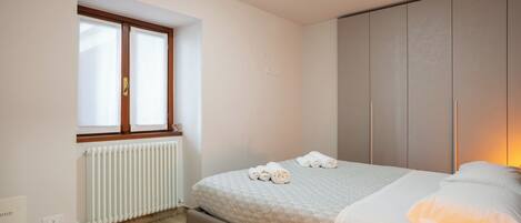 Un dormitorio con cama, ventana, radiador y armario.