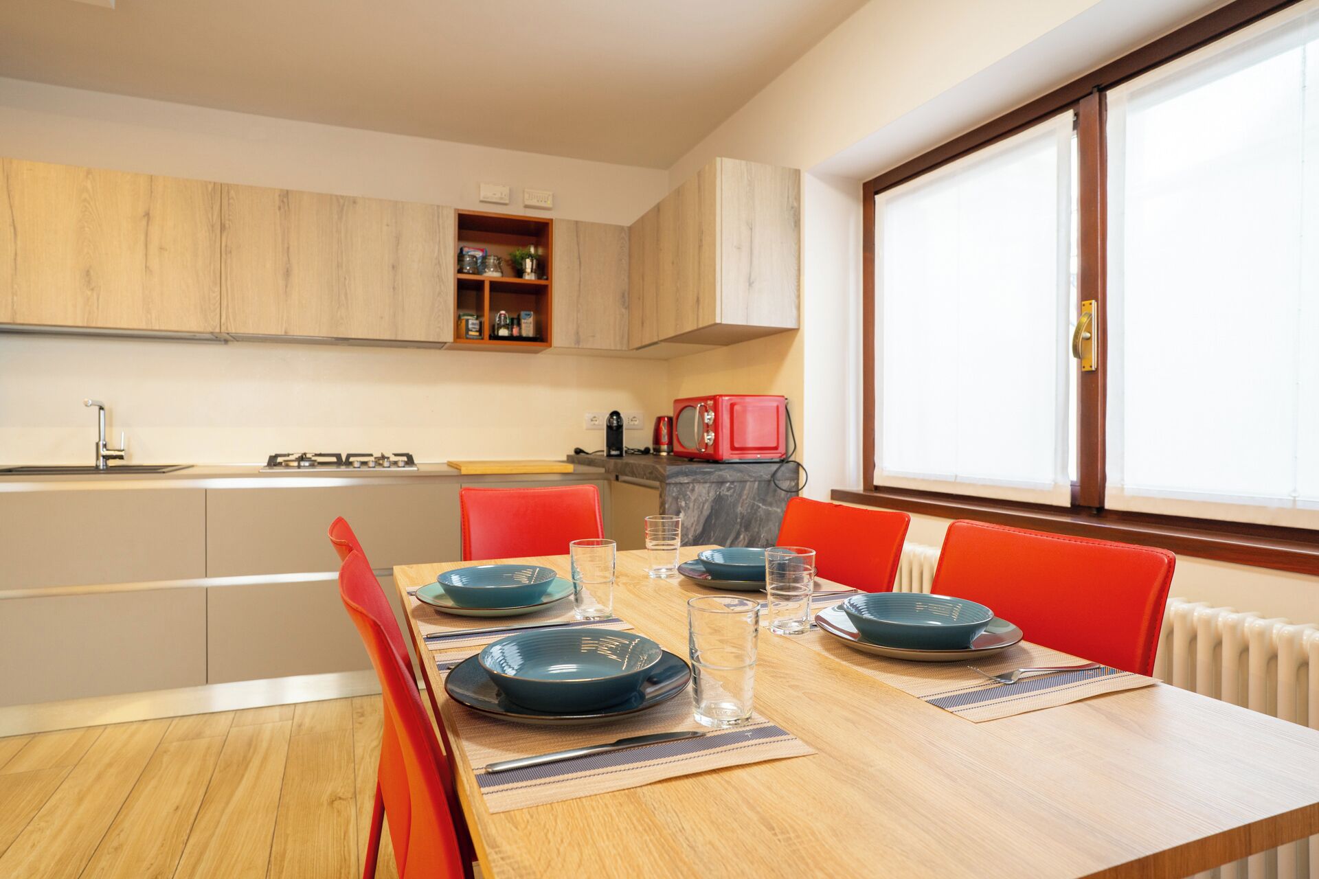 Une cuisine moderne avec des meubles en bois, un micro-ondes rouge et un coin repas comprenant une table en bois et des chaises rouges.