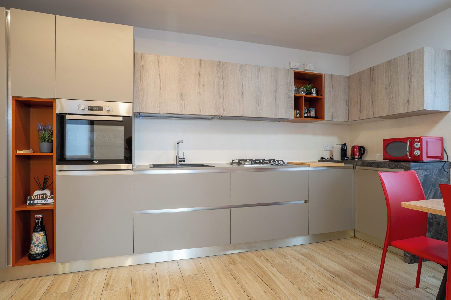 A modern kitchen with a built-in oven, microwave, and gas stove. There is a red chair and a small table. - Il Balcone in centro di Via Manzoni (Barzio)