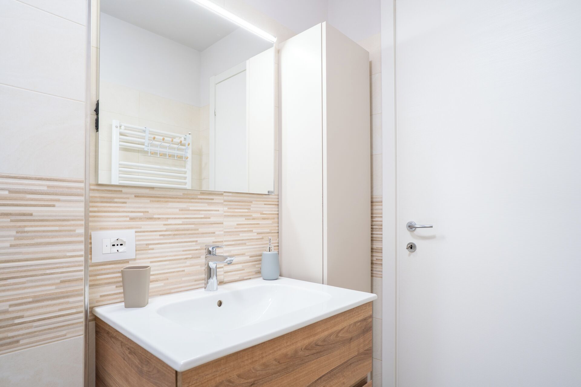 A modern bathroom with a white sink, wooden vanity, and a mirror.
