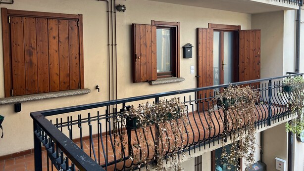 A multi-story building with wooden doors and windows, a balcony with a wrought iron railing, and a tiled roof. - Il Balcone in centro di Via Manzoni (Barzio)