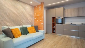 A modern kitchen with a built-in oven and microwave, a light blue sofa with colorful cushions, and a wooden floor. - Il Balcone in centro di Via Manzoni (Barzio)