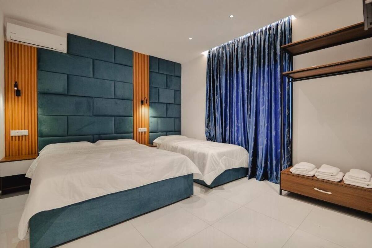 Une chambre d’hôtel avec deux lits, un mur lambrissé en bois, un rideau bleu et une commode en bois avec des serviettes.