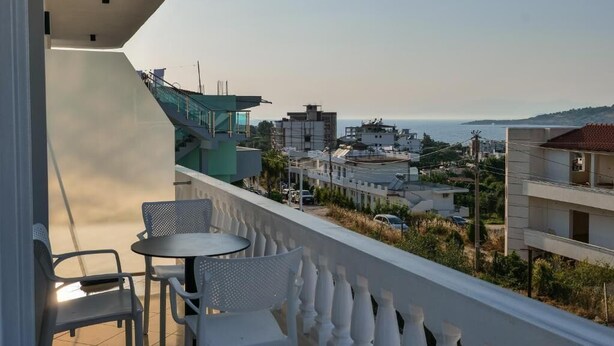 A balcony with a table and chairs, overlooking a coastal cityscape with buildings and a view of the sea. - Vila Eduart (Ksamil)