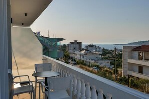 A balcony with a table and chairs, overlooking a coastal cityscape with buildings and a view of the sea. - Vila Eduart (Ksamil)