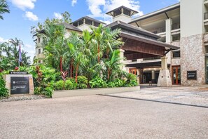 A hotel entrance with a stone facade, palm trees, and a sign for Pullman Palm Cove Sea Triangle Resort. - 234 Temple Tranquility: Triton Retreat- Luxury Palm Cove Apartment with Resort Pool & Oversized Balcony (Palm Cove)