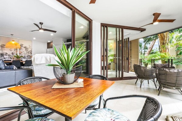 A dining area with a wooden table, chairs, and a potted plant. - 234 Temple Tranquility: Triton Retreat- Luxury Palm Cove Apartment with Resort Pool & Oversized Balcony (Palm Cove)