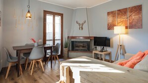 Een gezellige woonkamer met een open haard, een eethoek met stoelen en een tafel, en een tv op een dressoir.