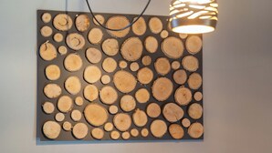 Een houten kunstwerk aan de wand met cirkelvormige patronen, een hanglamp en een tafel met een theepot.