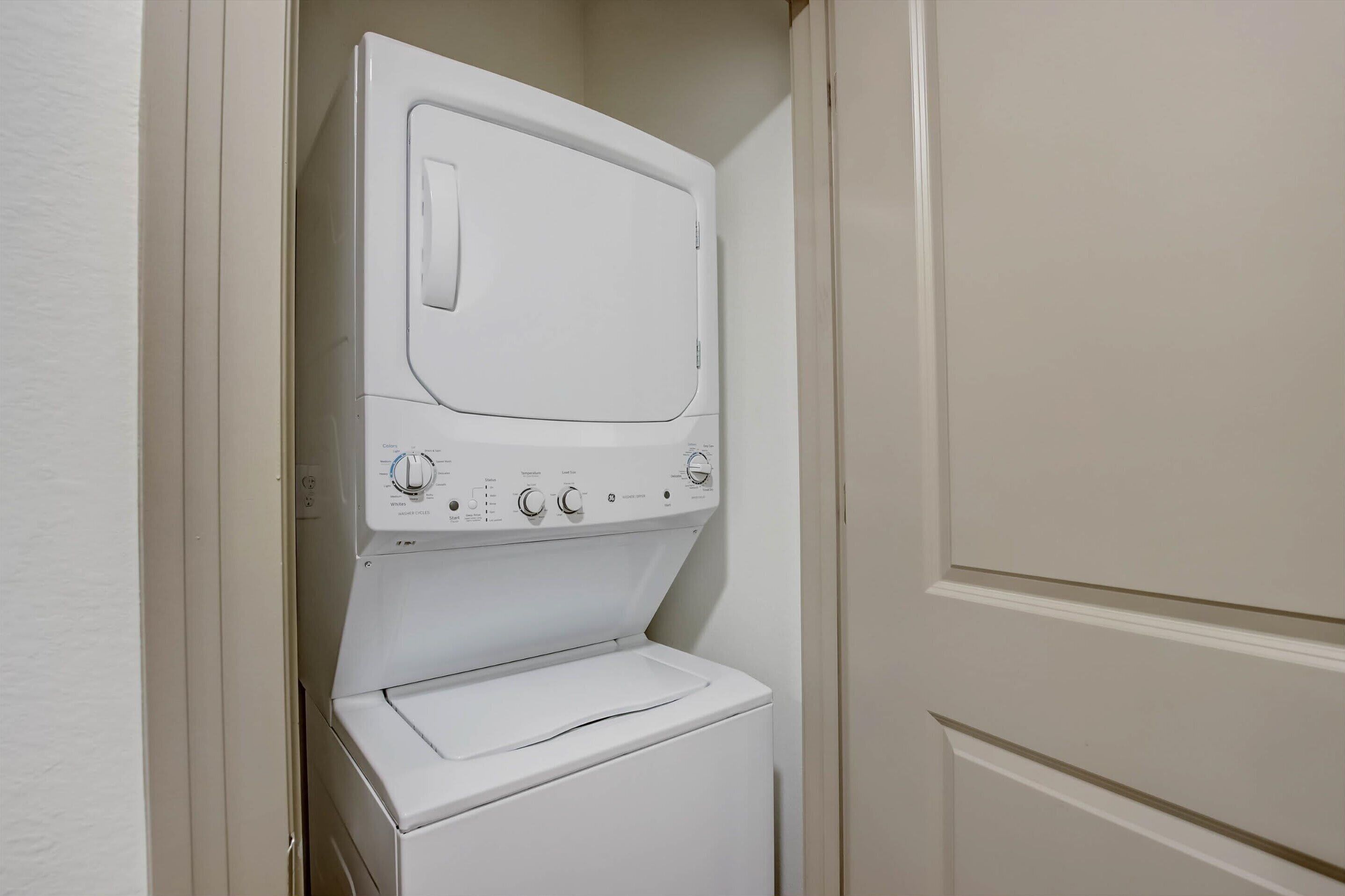 A white front-loading washer and dryer in a small laundry room with a door on the right.