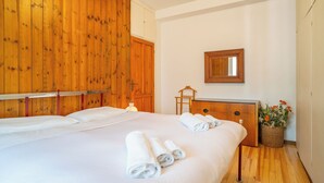 A hotel room with a wooden wall, a bed with white linens, a wooden dresser, a mirror, and a basket of flowers.