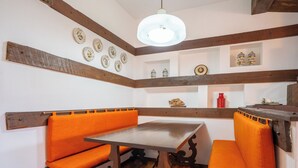 A dining area with wooden beams, a table, and orange cushioned benches.