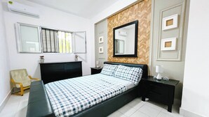 A bedroom with a bed, a nightstand, a chair, a dresser, a mirror, and a window with blinds. - Beautiful 3-bed Apartment in Kilamba - Luanda (Belas)