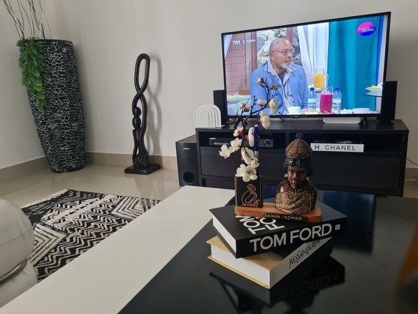 A modern living room with a flat-screen TV, a decorative vase with white flowers, a statue, and a book titled 'Tom Ford' on a black coffee table. - 5-bed Apartment Sleeps 10 - Wi-fi - Free Parking (Belas)