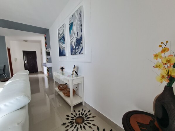 A modern living room with a white sofa, a glass coffee table, and a white console table with decorative items. There are two abstract paintings on the wall and a vase with yellow flowers on a table. - 5-bed Apartment Sleeps 10 - Wi-fi - Free Parking (Belas)
