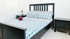 A bed with a checkered bedspread, a pillow, a nightstand with a lamp, and a drawer unit. - Remarkable 5-bed Apartment in Kilamba - Luanda (Belas)