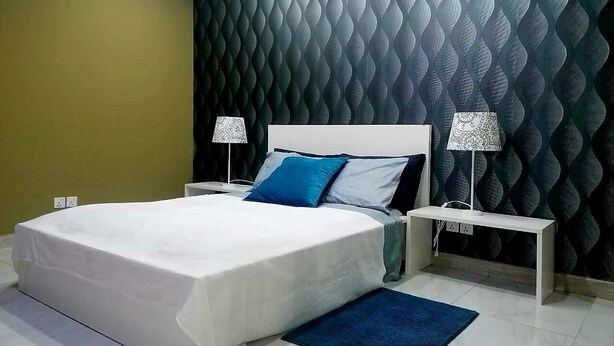 A modern bedroom with a bed, bedside tables, lamps, and a patterned wall. - Guest House Sleeps 14 With Terrace (Luanda)