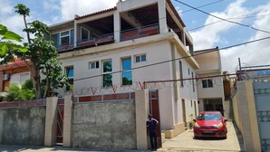 A two-story building with a balcony, a gated entrance, and a red car parked in front. - Guest House Sleeps 14 With Terrace (Luanda)