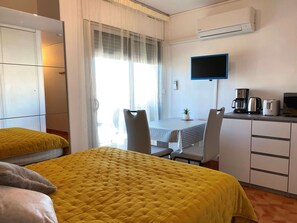 Habitación de hotel con cama, escritorio, silla, televisión y kitchenette.