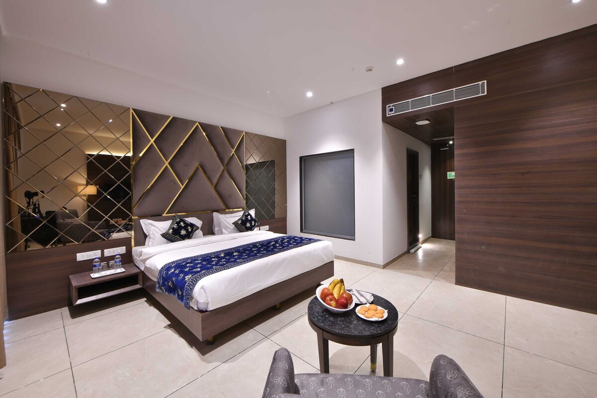 Een moderne hotelkamer met een groot bed, een nachtkastje met een schaal fruit, een klein rond tafeltje en een grote spiegel.