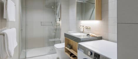 A modern bathroom with a glass-enclosed shower, a toilet, a washing machine, and a vanity with a mirror.