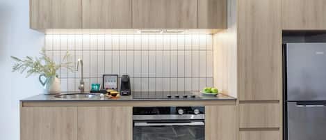 A modern kitchen with wooden cabinets, a stainless steel refrigerator, a built-in oven, and a tiled backsplash.